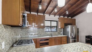 A kitchen with granite countertops, wooden cabinets, a stainless steel refrigerator, and a gas stove. - Bay Views Near the Beach with BBQ and Balcony (El Centenario)