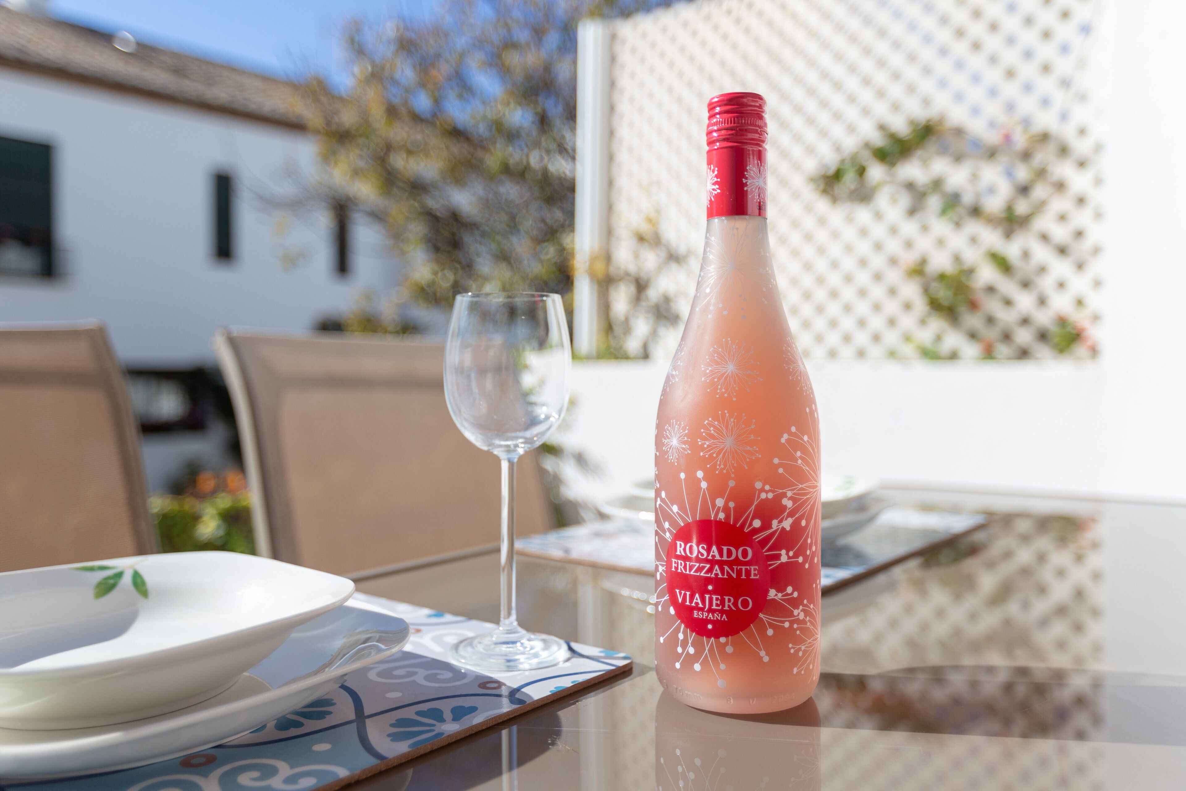 A table with a bottle of rosado frizzante, a glass, and a white plate on a patterned tablecloth.