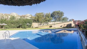 Una piscina con un muro de piedra y una estructura de techo de paja al fondo.