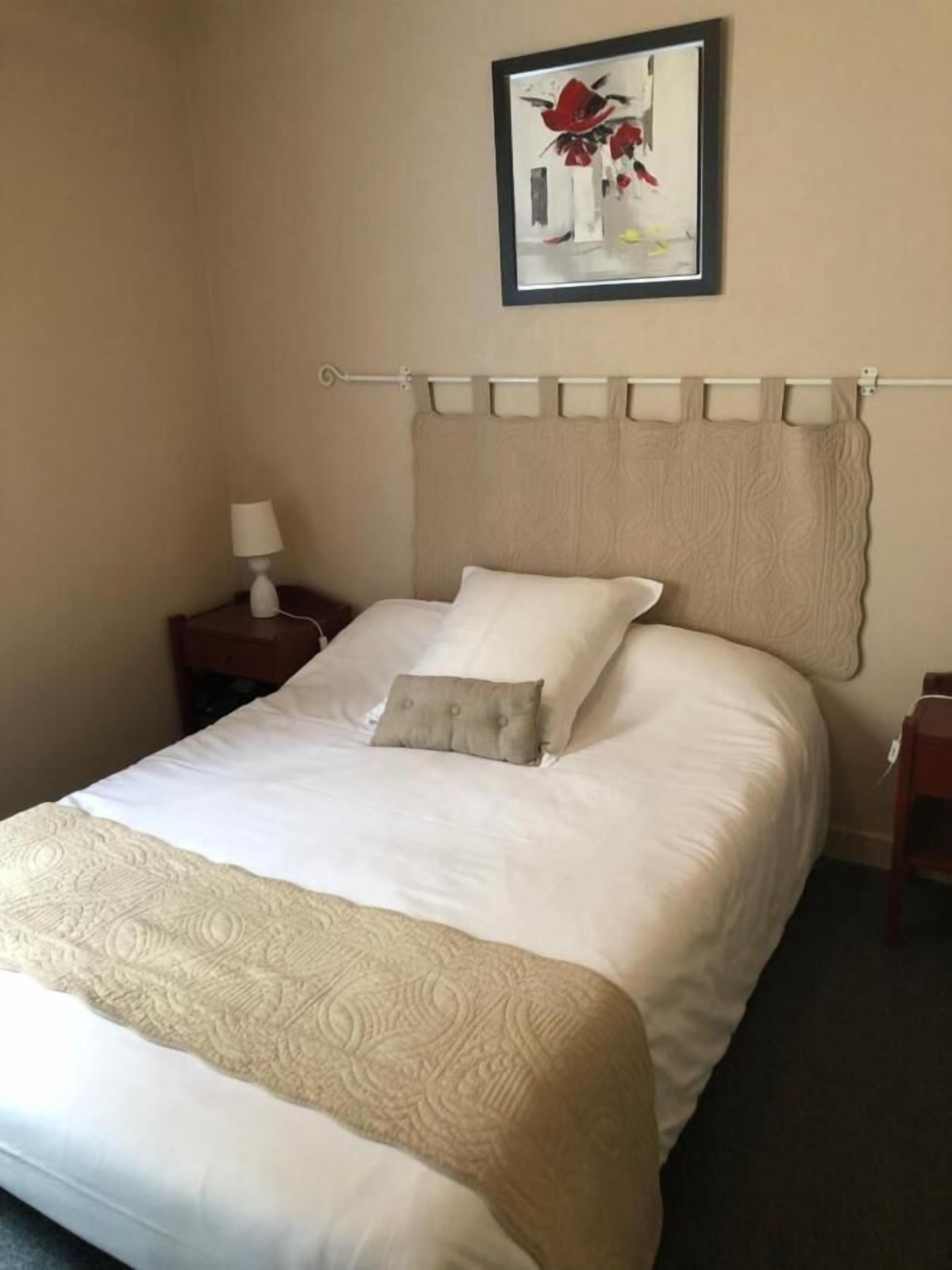 Una cama bien hecha con cabecera color crema, una sola almohada y una manta decorativa.