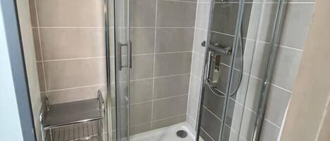 A corner shower with a glass door, a small shelf, and a yin-yang symbol on the wall.