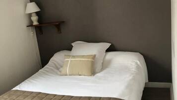 A neatly made bed with a quilted cover, a bedside lamp, and a small shelf with a lamp.