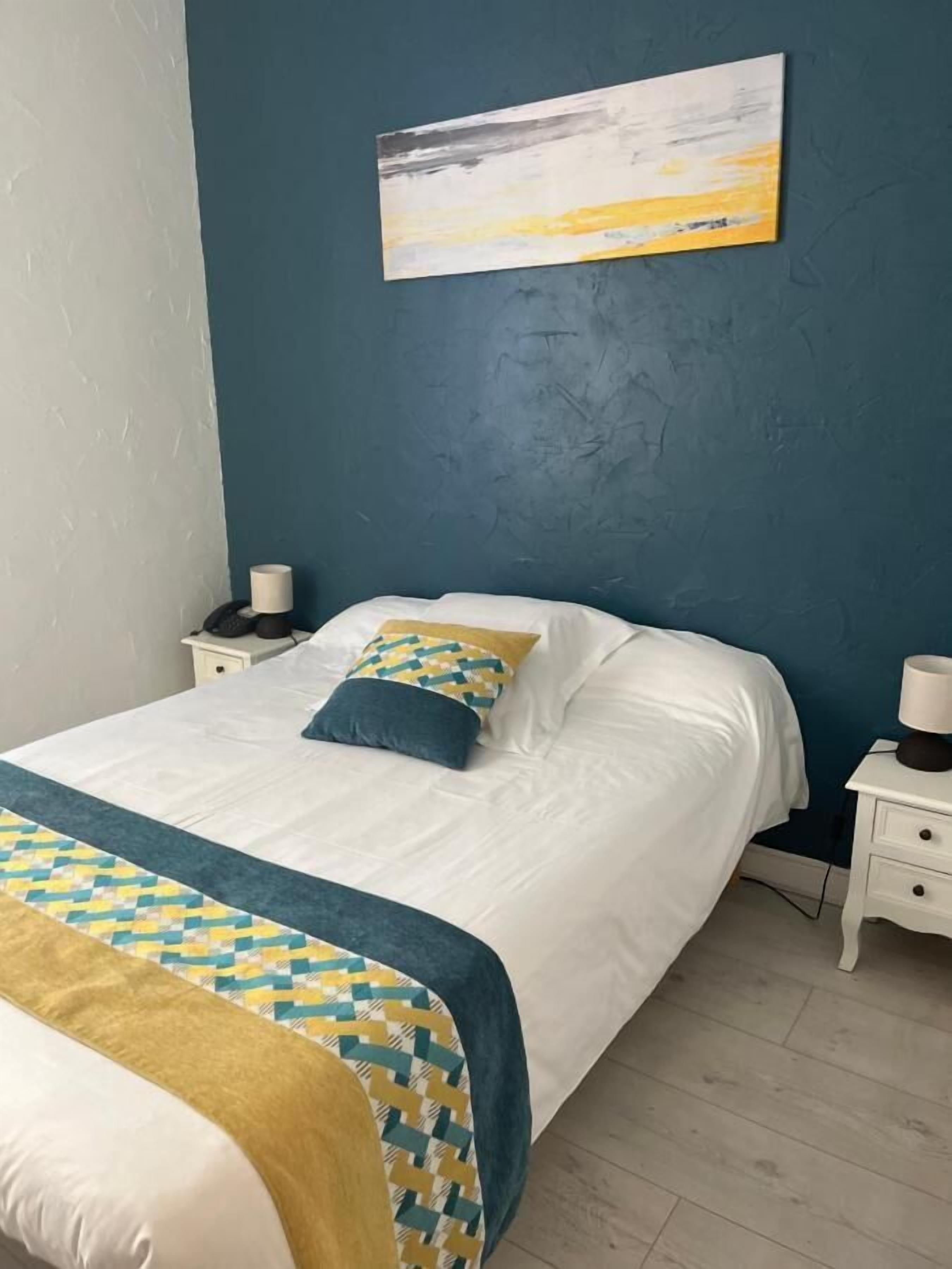 Un dormitorio con una cama, una mesita de noche con lámpara y un cuadro colgado en la pared.