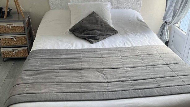 A neatly made bed with a grey quilt, white pillows, and a decorative heart on the wall. - Le Central Hôtel (Niort)