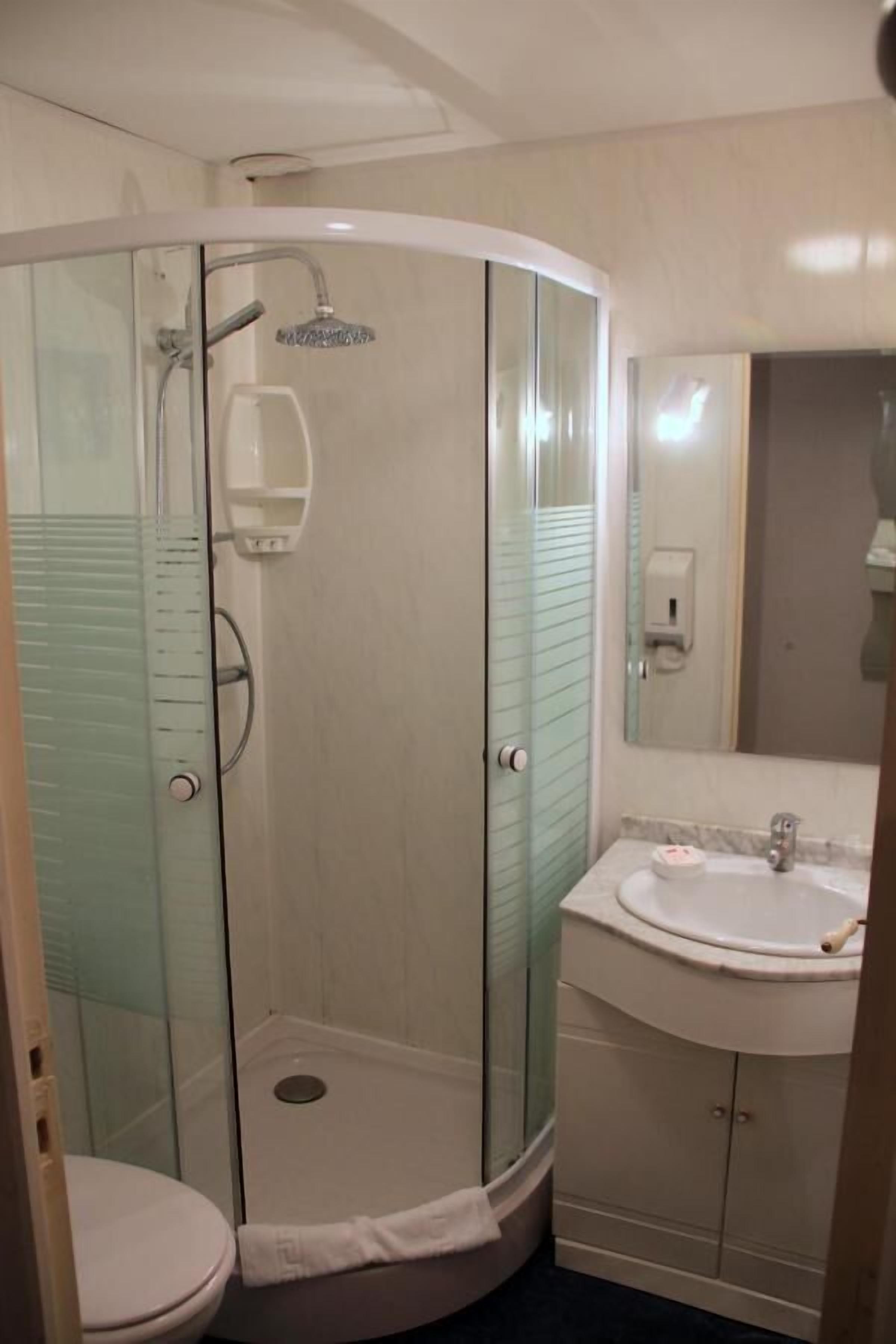 A bathroom with a glass-enclosed shower, a toilet, and a sink with a mirror.