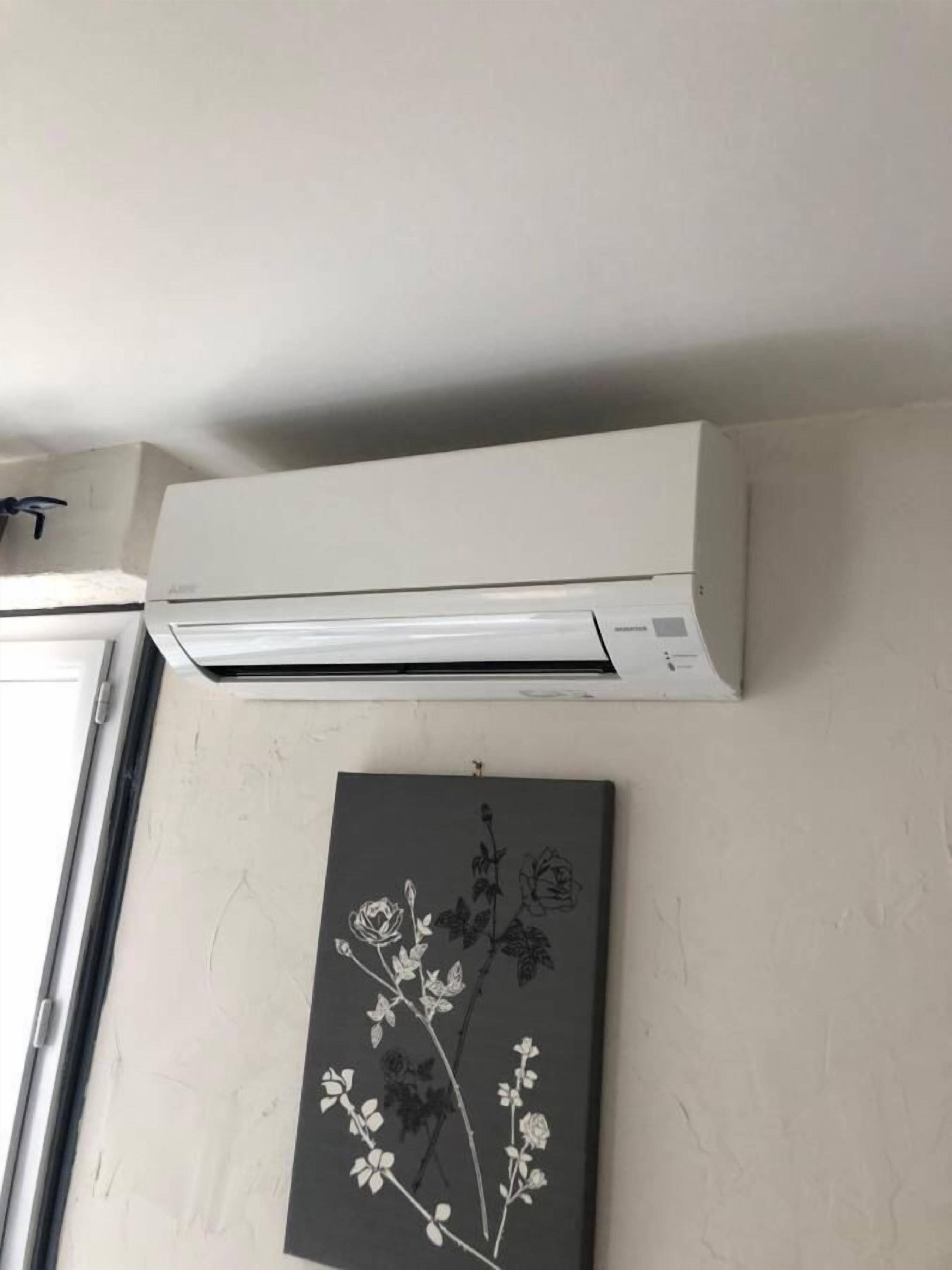 Un equipo de aire acondicionado blanco montado en una pared, con un cuadro floral blanco y negro debajo.