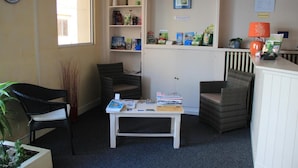 A room with two wicker chairs, a small table with books, a bookshelf with various items, and a window with natural light. - Le Central Hôtel (Niort)