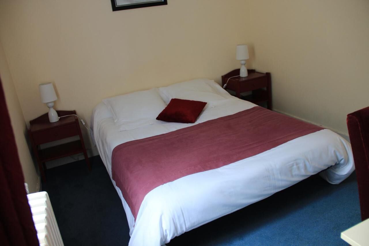 A hotel room with a single bed, a red pillow, two bedside tables with lamps, and a framed picture on the wall.