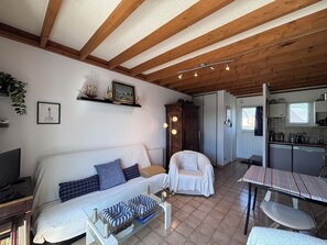 A cozy living room with a sofa, armchairs, a coffee table, and a kitchen area visible in the background.