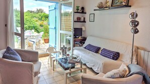 Une pièce confortable avec un canapé, deux fauteuils, une table en verre et un téléviseur. Une porte-fenêtre coulissante donne accès à un patio équipé d’une table et de chaises.