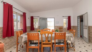 A dining area with a round table, six wooden chairs, and red curtains. - Villa Mausi in Chiclana de la Frontera (Chiclana de la Frontera)