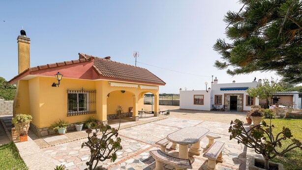 A yellow building with a red roof, a patio with stone tiles, and potted plants. - Villa Mausi in Chiclana de la Frontera (Chiclana de la Frontera)