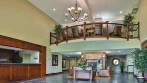 A spacious lobby with a high ceiling, a grand chandelier, a reception desk, and a staircase leading to an upper level. - 1 BDRM Condo - Great location - Hot tub and pool (Fernie)