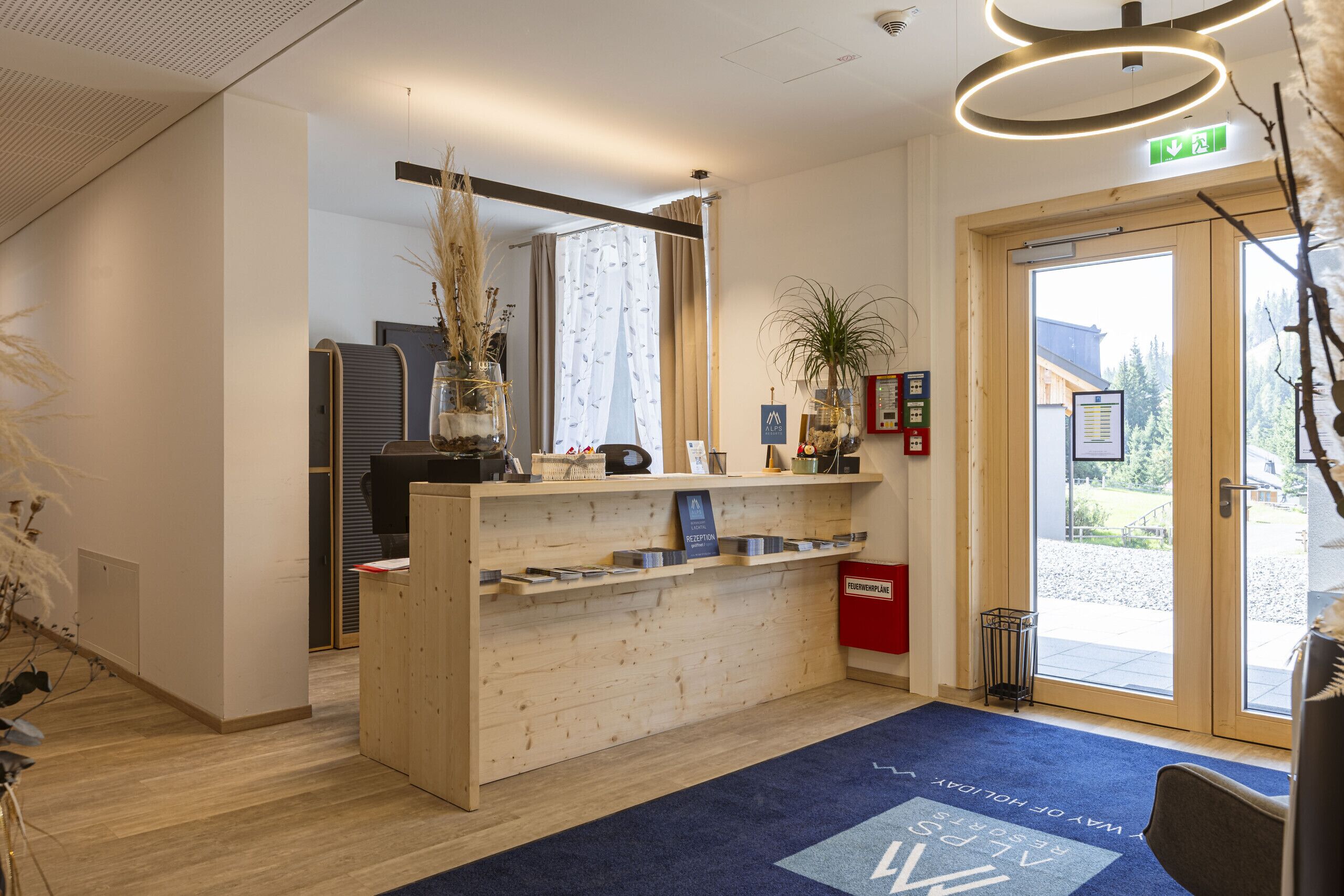 A reception desk with a blue carpet, a wooden counter, and a mirror above it.