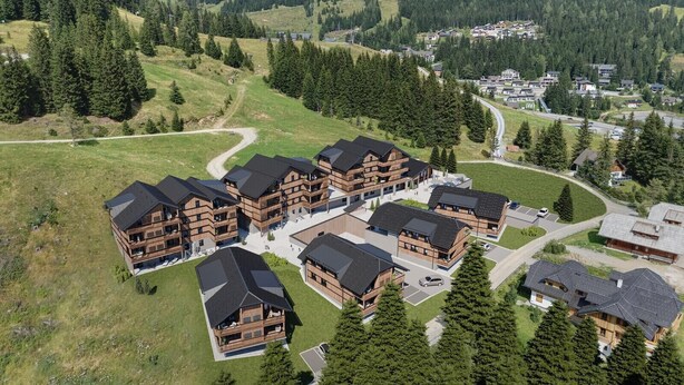 Un ensemble de bâtiments en bois dotés de nombreux balcons, entouré d’un paysage boisé et traversé par une route sinueuse.