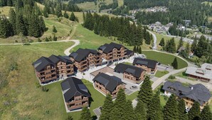 Un ensemble de bâtiments en bois dotés de nombreux balcons, entouré d’un paysage boisé et traversé par une route sinueuse.
