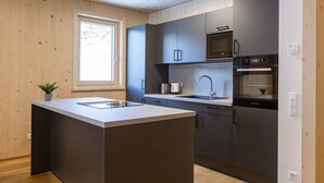 Une cuisine moderne dotée d’un îlot central, d’appareils électroménagers intégrés et de murs en bois.