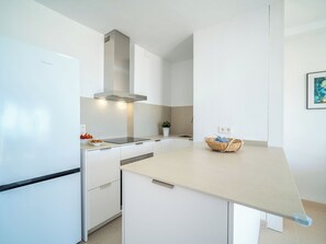 Una cocina moderna con armarios blancos, extractor de acero inoxidable y encimera de color claro.