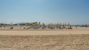 A beach with numerous sun loungers and umbrellas, a clear sky, and a few boats in the background. - Apartment Xisca by Interhome (Port d'Alcúdia)