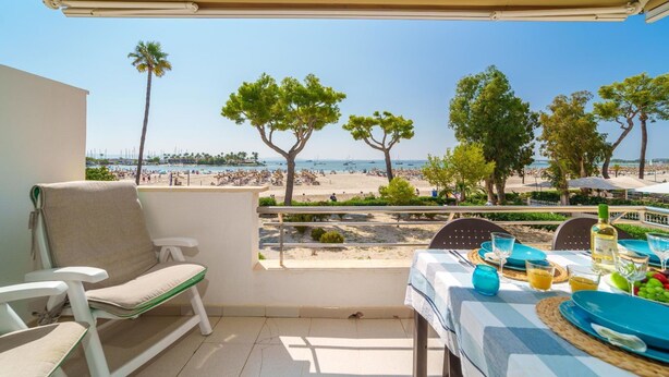 A balcony with a table set for dining, overlooking a beach with trees and boats. - Apartment Xisca by Interhome (Port d'Alcúdia)
