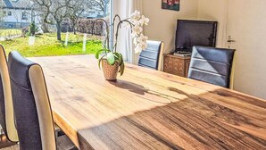 Ein Essbereich mit einem Holztisch, Stühlen, einer Orchidee im Topf und einem Fernseher.