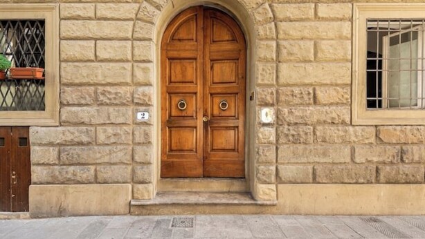 Un edificio de piedra con una puerta de madera doble, una ventana con reja de metal y un pequeño ventanal con barra de metal.