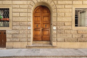 A stone building with a double wooden door, a window with a metal grille, and a small window with a metal bar. - Lilac - Milù Holidays Florence (Firenze)