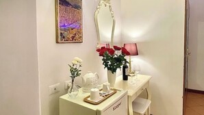 Una habitación con un tocador blanco, un espejo, un cuadro en la pared y un florero con flores rojas.
