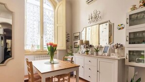 Un comedor con una mesa y sillas de madera, un armario blanco con puertas de vidrio y una ventana con cortinas.