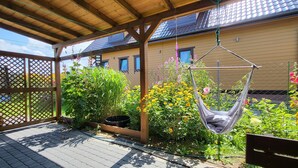A covered patio with a hammock, wooden deck, and a garden with various plants and flowers.