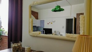 Une pièce avec un grand miroir, une lampe suspendue verte, une table en bois agrémentée d’un coussin décoratif et une petite plante.