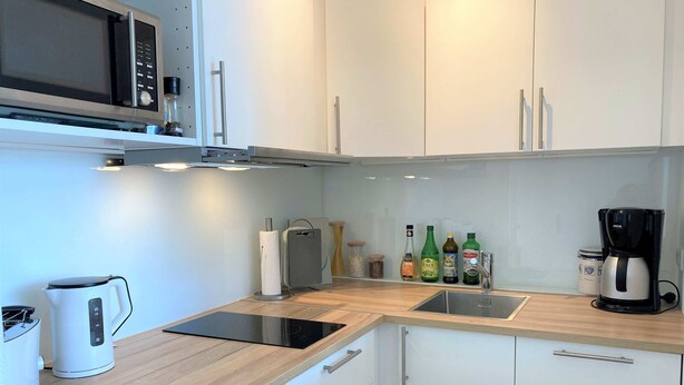 A modern kitchen with white cabinets, a microwave, a kettle, a coffee maker, and various bottles on the counter. - A little time out for relaxing days... Close to the beach and the center! (Dahme)