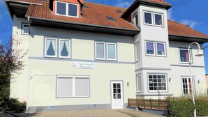 A two-story building with a light facade, multiple windows, and a sign indicating it is a residential property. - A little time out for relaxing days... Close to the beach and the center! (Dahme)