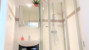 A modern bathroom with a glass-enclosed shower, a white sink with a black cabinet, and a mirror above the sink. - A little time out for relaxing days... Close to the beach and the center! (Dahme)