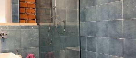 Un baño moderno con cabina de ducha de vidrio, un lavabo blanco y una pared de ladrillo a la vista.