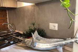 Una cocina con una escultura de acero inoxidable con forma de pez sobre la encimera, una estufa a gas, un lavaplatos y una planta en maceta.