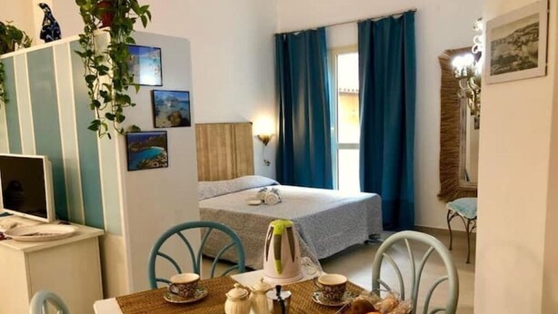 Um quarto aconchegante com uma cama, uma escrivaninha com um computador, uma mesa de jantar com cadeiras e uma janela com cortinas.