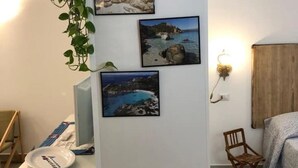 Quarto com escrivaninha, cadeira, luminária na parede e quadros de paisagens costeiras.