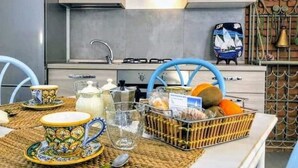 Cozinha com coifa de aço inoxidável, torneira azul e cesta de frutas e legumes no balcão.