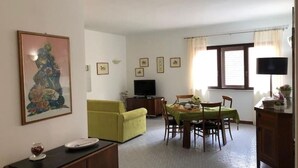 En matplats med ett bord dukat för två personer, en grön soffa, en tv och inramade tavlor på väggen.