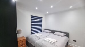 A bedroom with a bed, a nightstand, a lamp, and a window with blinds. - Enjoyable 3-bedroom house with WiFi in Watford central / 30min to Central London (Watford)