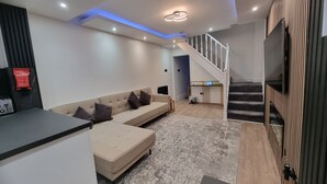 A modern living room with a sofa, a small table, a staircase, and a TV mounted on the wall. - Enjoyable 3-bedroom house with WiFi in Watford central / 30min to Central London (Watford)