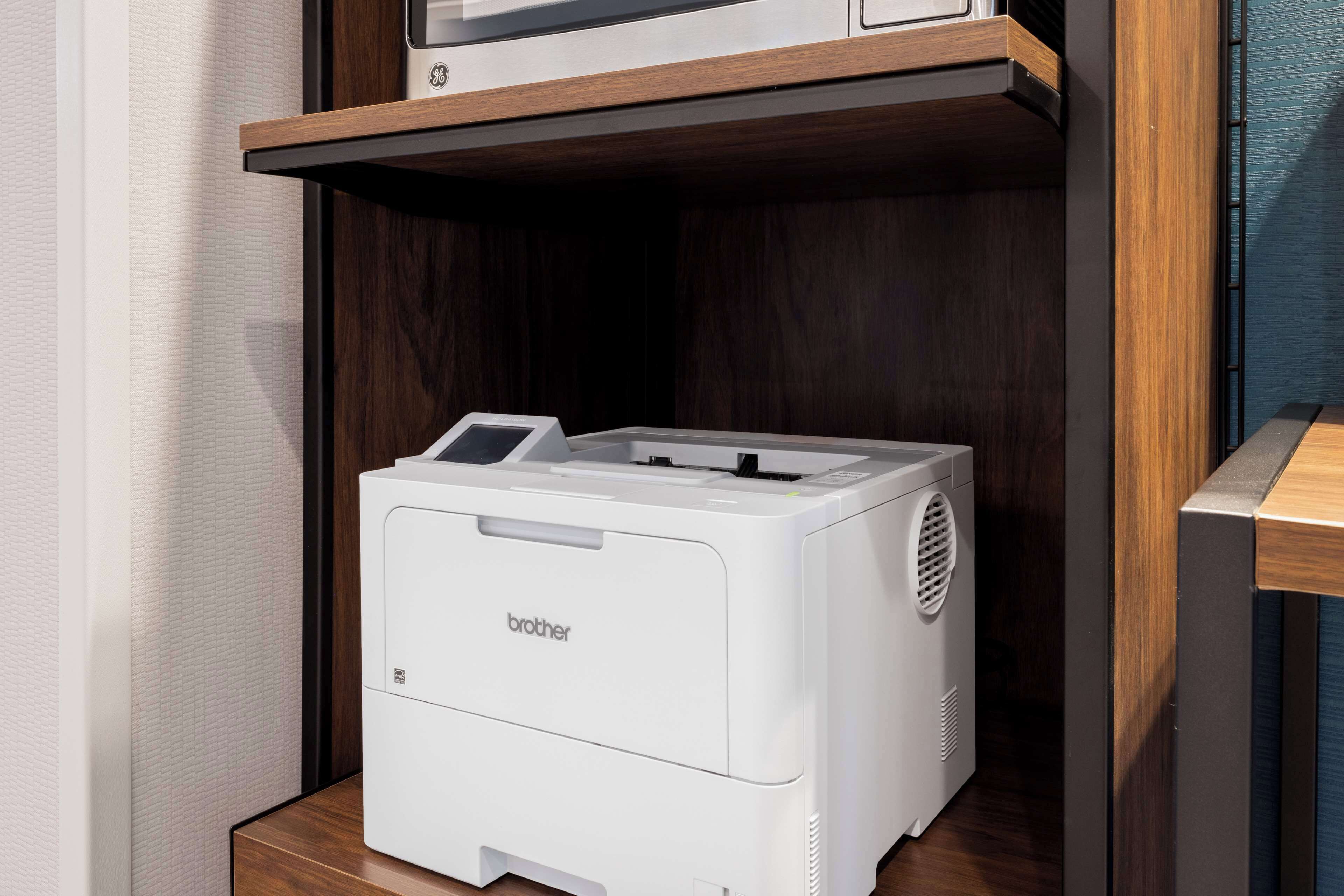 A Brother printer on a wooden shelf in a room with dark wood paneling.