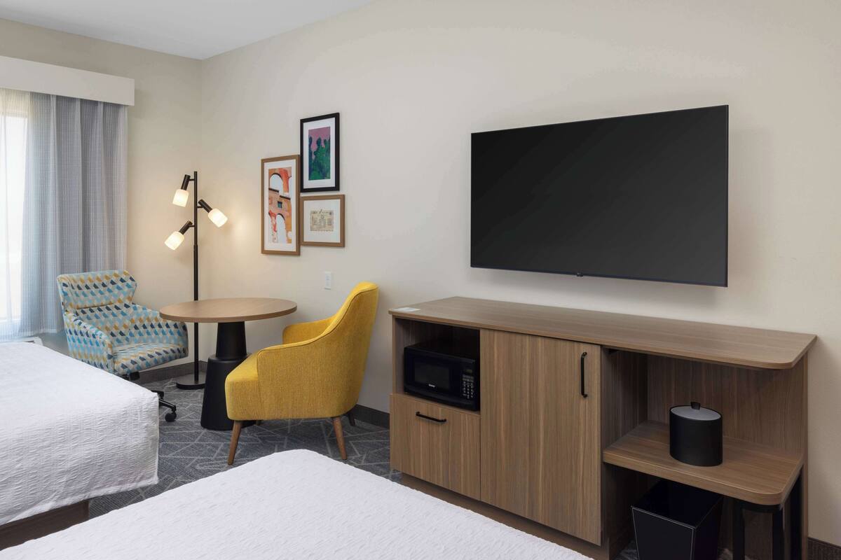 Habitación de hotel con dos camas, un escritorio, una silla, un televisor de pantalla plana y un microondas.