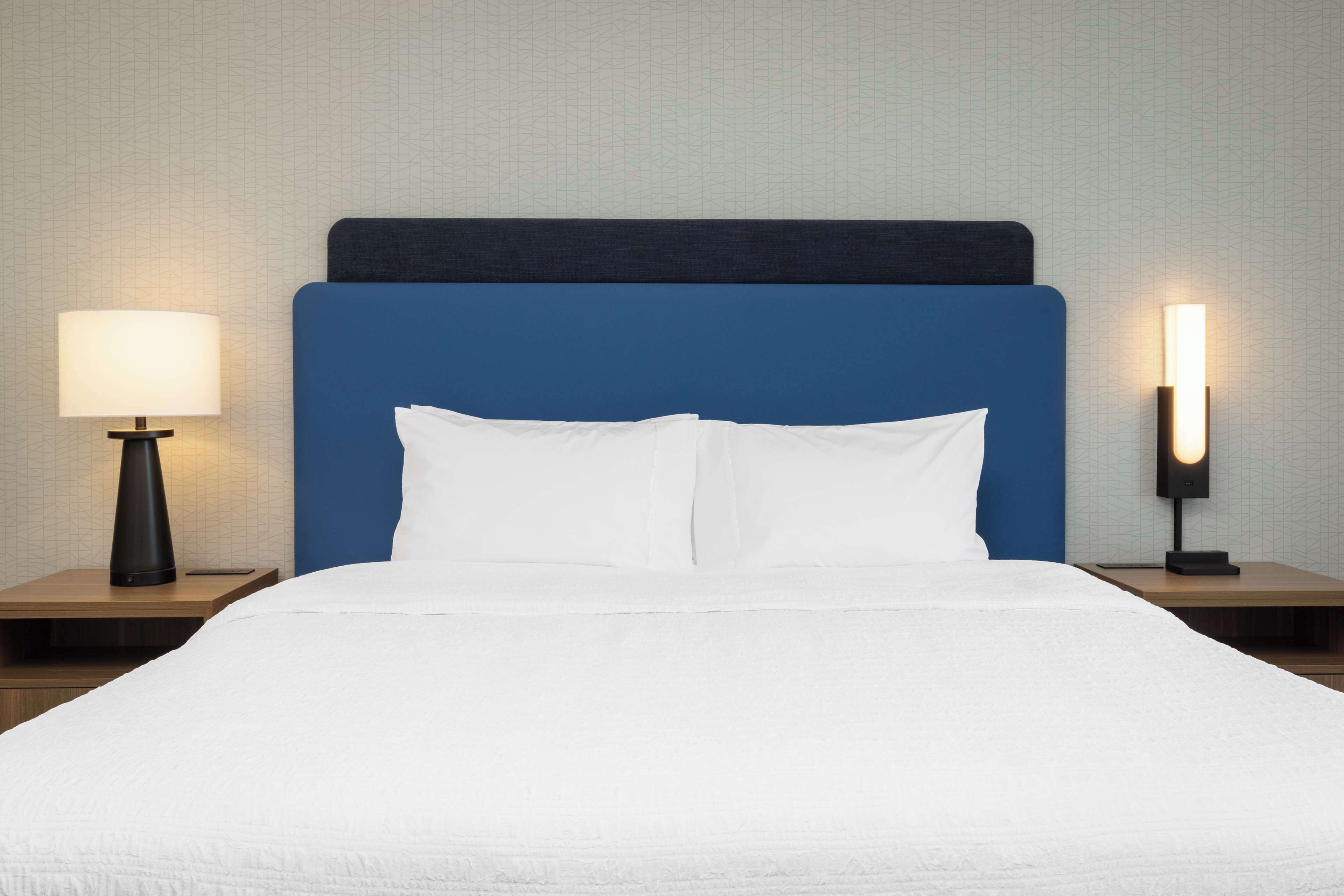 Un lit bien fait, avec une tête de lit bleue, deux tables de chevet avec des lampes et un mur texturé en arrière-plan.