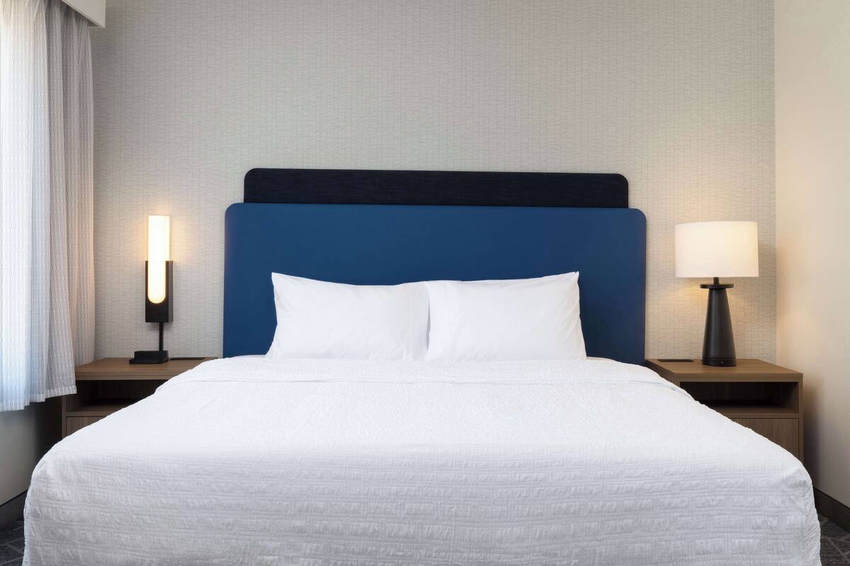 Una habitación de hotel con una cama grande, dos mesitas de noche y una lámpara.