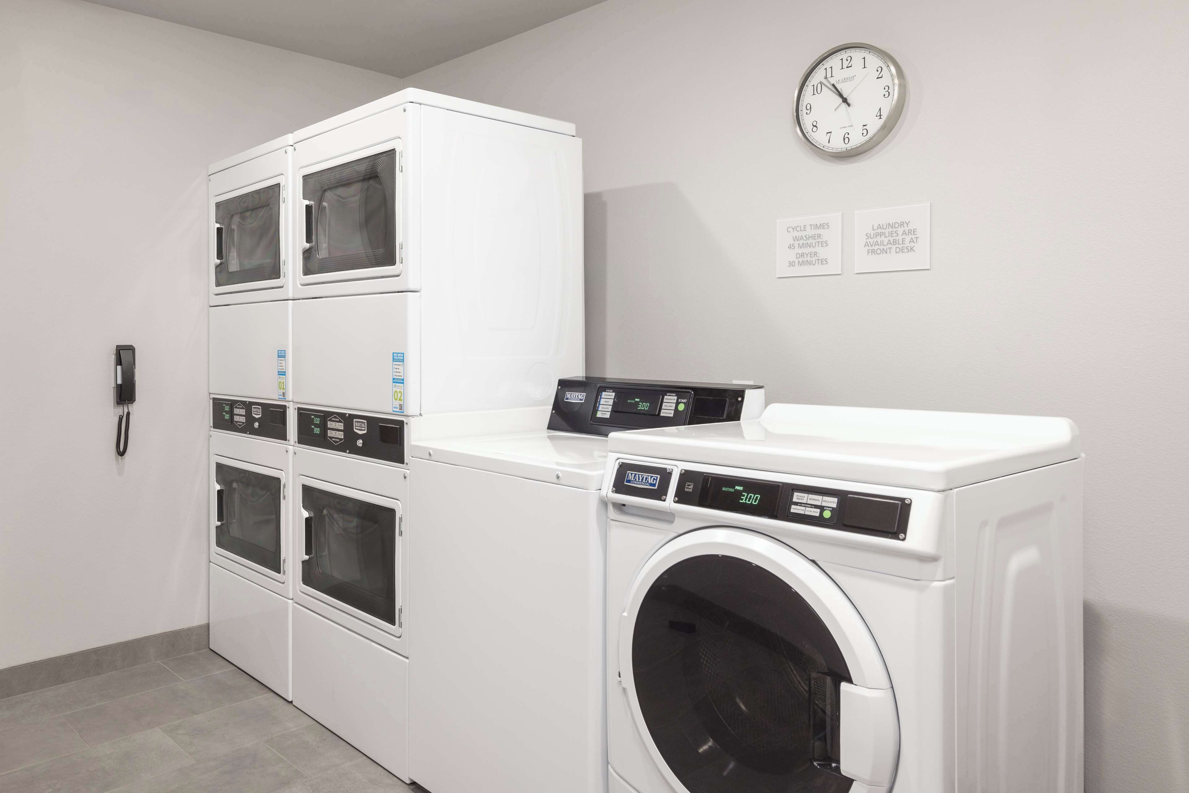A laundry room with stacked dryers, a front-loading washer, and a clock on the wall.