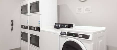A laundry room with stacked dryers, a front-loading washer, and a clock on the wall.