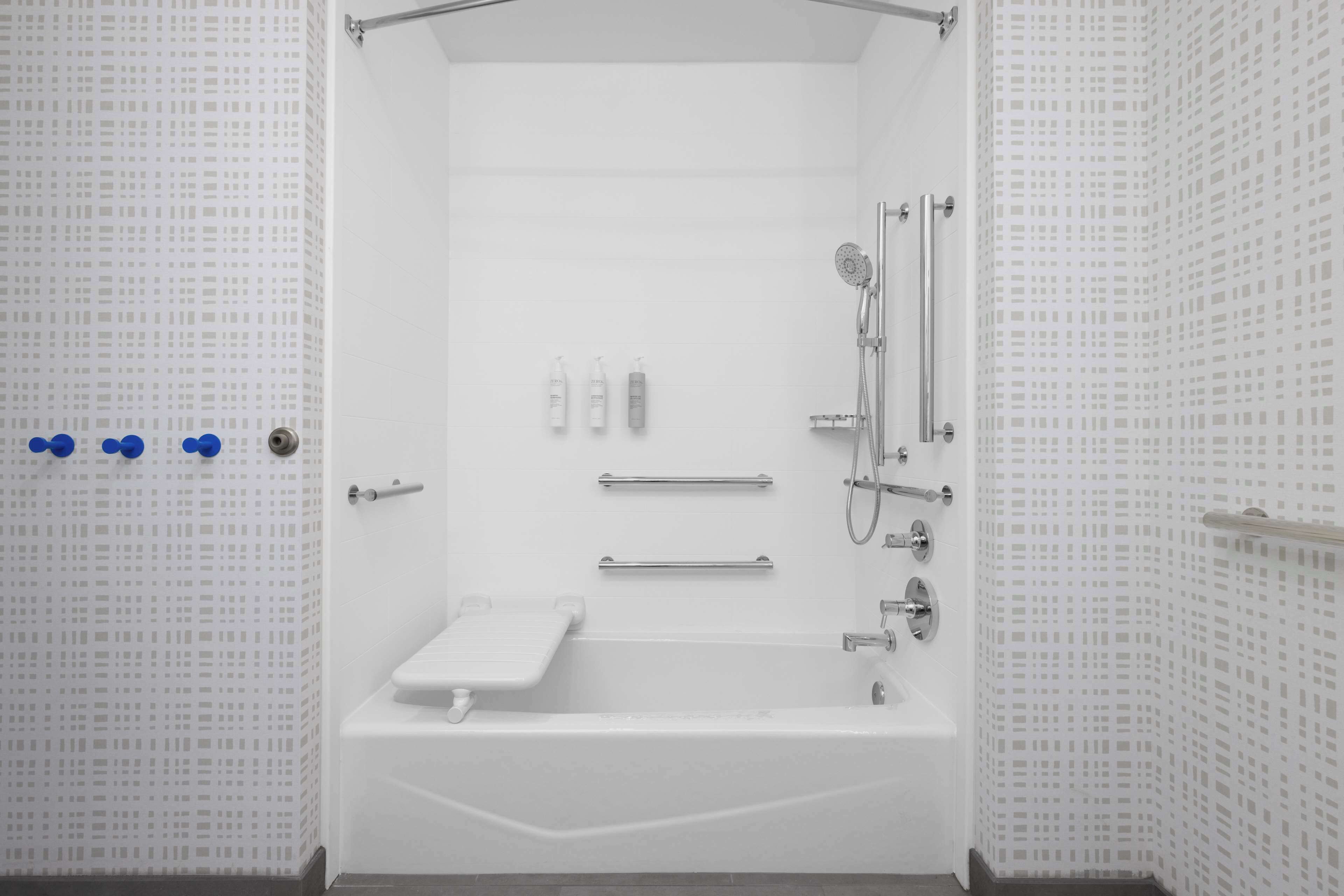 A modern bathroom with a bathtub, shower, and handrails.