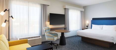 A hotel room with a bed, a sofa, a chair, a TV, and a desk.